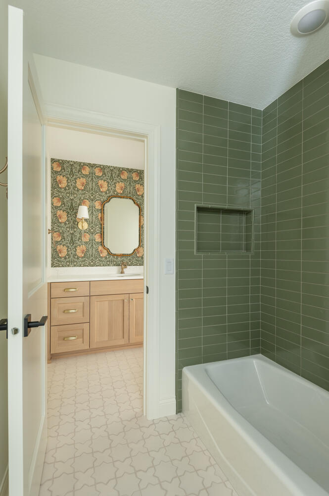 Modern bathtub and shower leading to room with vanity, brass fixtures, and floral wallpaper